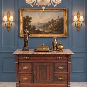 May include: A dark wood sideboard with a marble top, featuring four drawers and a central cabinet door with brass hardware. On top sits a bronze statue, a rectangular metal box on a tray, a tall brass vase, and a lidded brass jar.