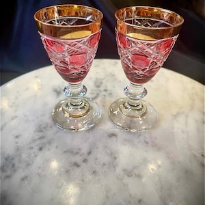 Puede incluir: Dos copas de vino de cristal rojo rubí con bordes dorados. Las copas tienen un patrón de corte de diamante y se apoyan en tallos y bases transparentes. Adecuadas para servir vino u otras bebidas.