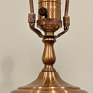 May include: Close-up of a vintage table lamp with a pink and black patterned base and a brass-colored metal body. The lamp has a bulb socket and a switch. The lamp is designed for indoor use.