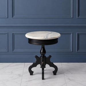 May include: A round side table featuring a white and grey veined marble top set upon a black wooden base. The table has a single central pedestal column that branches into three curved legs, providing a stable foundation for the circular surface.