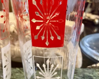 May include: Two clear glass tumblers with a red and white geometric snowflake design. The glasses are perfect for serving beverages.