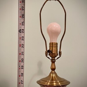 May include: A vintage table lamp with a pink bulb and a brass base. The lamp has a floral design on the base and stands approximately 16 inches tall.