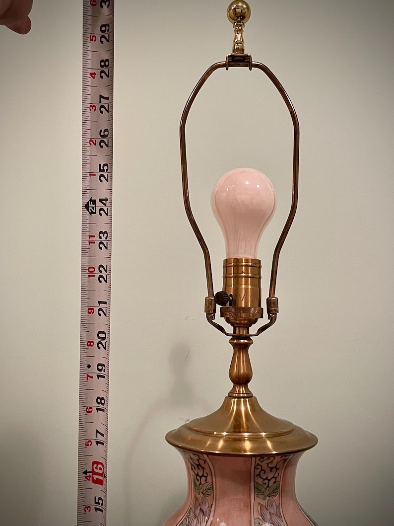 May include: A vintage table lamp with a pink bulb and a brass base. The lamp has a floral design on the base and stands approximately 16 inches tall.