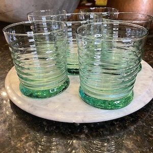 Puede incluir: Juego de seis vasos transparentes con diseño acanalado. La base de cada vaso tiene un tinte verde. Los vasos están dispuestos sobre una bandeja de mármol blanco. Ideales para servir agua, zumo o cócteles.
