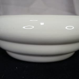May include: A white ceramic bowl with a glossy finish. The bowl has a rounded shape with three stacked, tiered sections. The bowl is on a black surface. The bowl is likely used for serving food or as a decorative item.