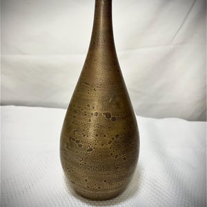 May include: A bronze-colored, teardrop-shaped vase with a narrow neck. The surface has a textured, speckled appearance. The vase is displayed against a white background, highlighting its unique shape and color. This decorative vase is suitable for home decor.