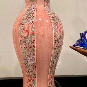 May include: A pink ceramic table lamp with a brass base and top. The lamp features a floral design with pink and purple lotus flowers and green leaves. The lamp is approximately 20 inches tall.
