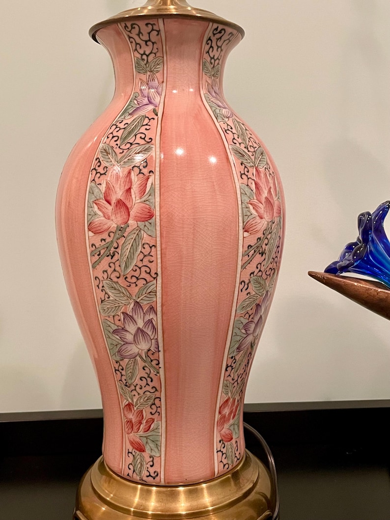 May include: A pink ceramic table lamp with a brass base and top. The lamp features a floral design with pink and purple lotus flowers and green leaves. The lamp is approximately 20 inches tall.