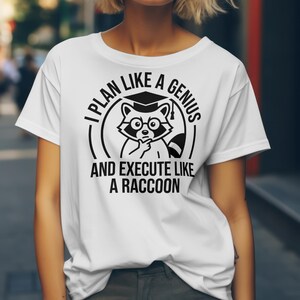 May include: White t-shirt with a black graphic of a raccoon wearing glasses and a graduation cap. The text reads "I PLAN LIKE A GENIUS AND EXECUTE LIKE A RACCOON."