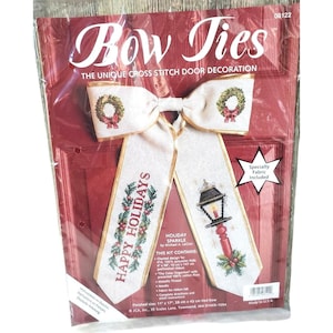 May include: A cross-stitch kit for a Christmas door decoration. The kit includes a large bow with the words "Bow Ties" at the top. The bow is white with gold trim and features a wreath and a lamp post design. The words "Happy Holidays" are also visible.