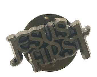 May include: A silver-colored pin with the words "JESUS FIRST" in a stylized font. The pin features a cross at the end of the word "FIRST". The pin is circular in shape.