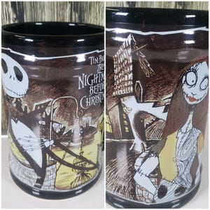 May include: Black ceramic mug featuring characters and scenes from "The Nightmare Before Christmas." The mug has a black rim and base, with illustrations of Jack Skellington and Sally. The mug also has the movie title printed on it.