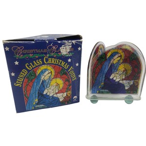 May include: A stained glass Christmas votive candle holder with a blue box. The candle holder features a depiction of Mary and baby Jesus in a stained glass design with red, blue, and yellow hues. The box reads "Stained Glass Christmas Votive".