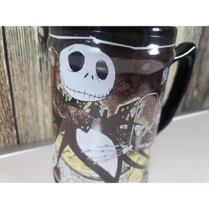 May include: A black coffee mug featuring Jack Skellington from The Nightmare Before Christmas. The mug has a black handle and a detailed illustration of Jack in his signature pose, with a spooky background.