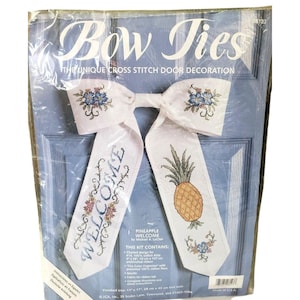 May include: A cross-stitch kit for a door decoration. The kit includes a white bow with the text "WELCOME" and a pineapple design. The finished size is 11" x 17" (28 cm x 43 cm).