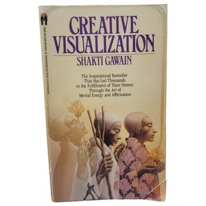 May include: A paperback book titled Creative Visualization by Shakti Gawain with a cream-colored cover. The front features an illustration of three figures in profile, holding flowers and sticks, with purple text and a small logo in the top corner.