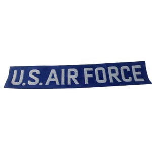 May include: A blue rectangular patch with the text "U.S. AIR FORCE" in white block letters. The patch is made of a woven material and is likely designed to be sewn onto clothing or gear.
