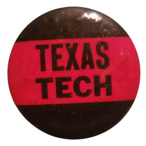 May include: A round button with a black outer ring and a red center band. The words "TEXAS TECH" are printed in bold black letters across the red band. The button has a slightly worn appearance.