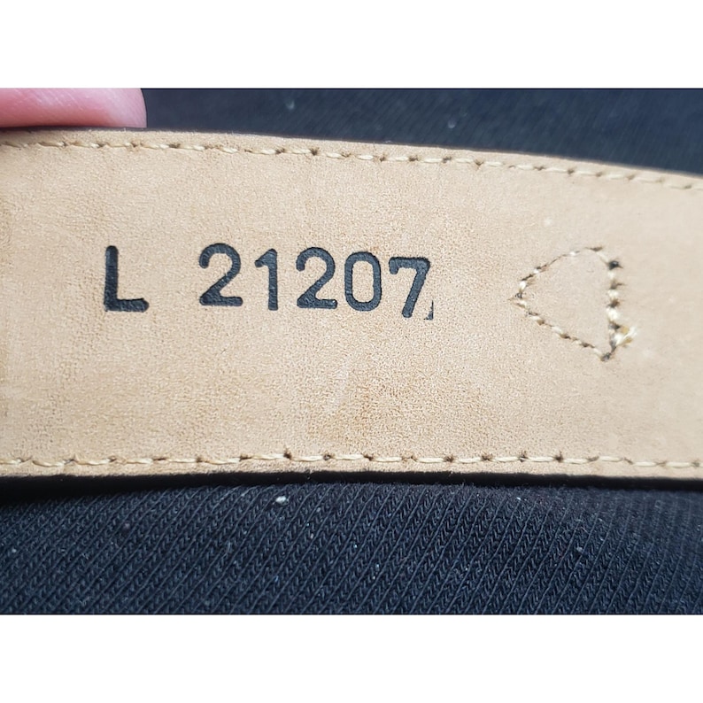 May include: Close-up of a brown leather belt tag with the text "L 21207" printed in black.