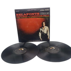 May include: A vintage vinyl record album titled "Belafonte Returns to Carnegie Hall" with a red and black cover featuring a portrait of a man. Two black vinyl records are in the foreground.