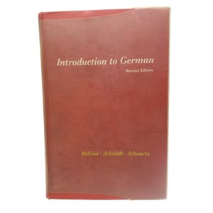 May include: A red book titled "Introduction to German" with the subtitle "Revised Edition." The book's cover features the names "DeVries, Schmidt, Schwartz" at the bottom. The book has a slightly worn appearance.