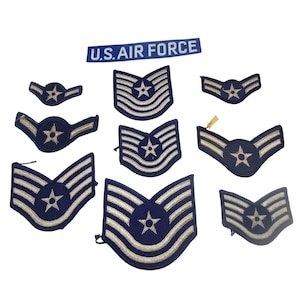 May include: A collection of U.S. Air Force patches and insignia. The patches are primarily navy blue with white stripes and star emblems. The text "U.S. AIR FORCE" is displayed on a blue patch.