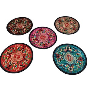 May include: Five embroidered oval coasters in various colors: red, brown, pink, tan, and teal. Each coaster features a central design with floral and geometric patterns, outlined in black.