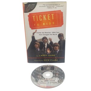 May include: A book titled Ticket to Ride by Larry Kane, featuring a photograph of The Beatles on the cover with the subtitle Inside the Beatles' 1964 Tour that Changed the World. The book includes a circular compact disc with matching text.