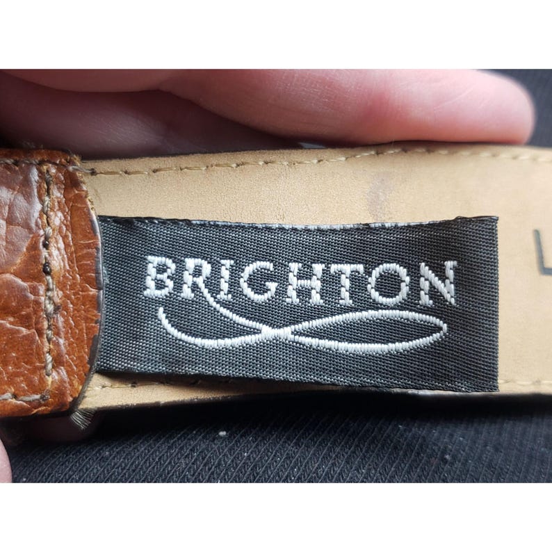 May include: A brown leather belt with a black label that says "BRIGHTON" in white lettering.