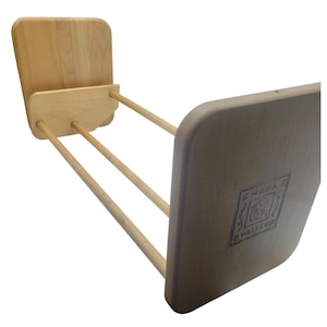 May include: A light-colored wooden drying rack with a rectangular base and two upright panels. Three dowels connect the base to the panels. The rack has a natural wood finish and is designed for drying clothes.