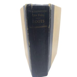 May include: A vintage hardcover book titled "Roots" by Alex Haley. The spine is dark blue with gold lettering, and the book's edges are beige. The book shows signs of wear, suggesting it is a well-loved edition.