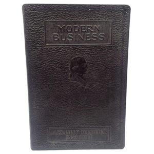 May include: A dark brown book with the title "MODERN BUSINESS" embossed on the cover. Below the title is a silhouette of a person's profile. The text "ALEXANDER HAMILTON INSTITUTE" is at the bottom.