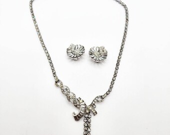 Op de afbeelding: Een zilveren ketting met een kristallen strik hanger en bijpassende kristallen oorbellen. De ketting heeft een delicate ketting en de hanger is versierd met heldere kristallen.