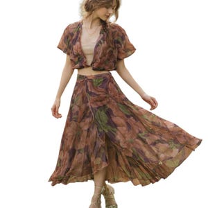 May include: A two-piece floral print outfit featuring a cropped, short-sleeved top and a flowing maxi skirt. The outfit has a brown, green, and purple color palette. The skirt has a high slit and a wrap design.