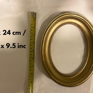 May include: Oval gold-coloured picture frame. The frame measures 19 x 24 cm and 7.5 x 9.5 inches. The frame is made of a solid material and has a smooth, rounded edge. The frame is empty.