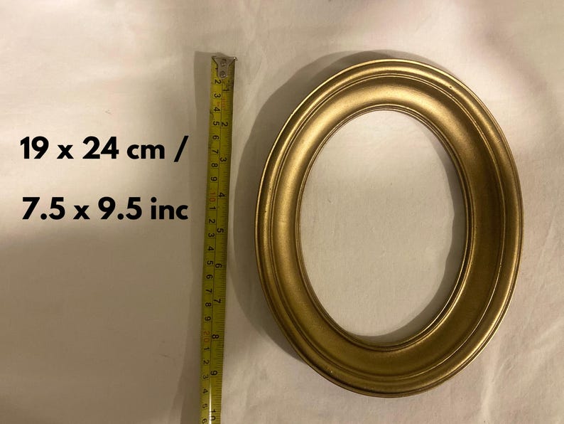 May include: Oval gold-coloured picture frame. The frame measures 19 x 24 cm and 7.5 x 9.5 inches. The frame is made of a solid material and has a smooth, rounded edge. The frame is empty.