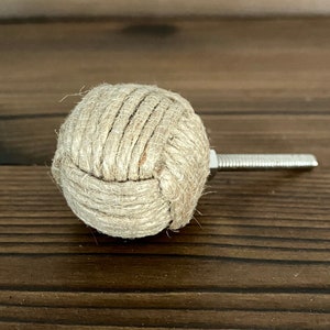 May include: A spherical cabinet knob made from natural-coloured rope, with a silver-coloured screw. The rope is tightly wound, creating a textured, knotted appearance. The screw is attached to the back for easy fitting. The knob is approximately 4 cm in diameter.