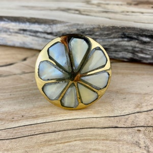 May include: A round brass knob with a white mother of pearl inlay in a flower design.