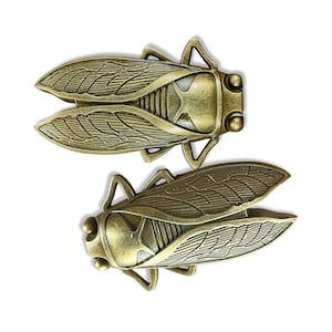 May include: Two gold-toned metal cicada brooches with detailed wings and bodies.