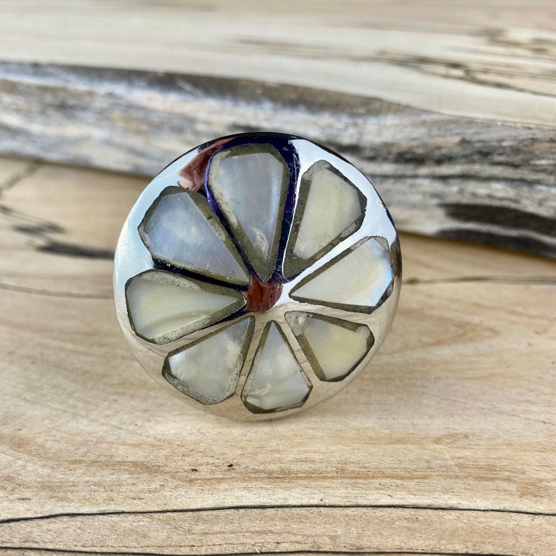 May include: A round, silver-toned cabinet knob with a white, mother-of-pearl inlay in the shape of a flower.