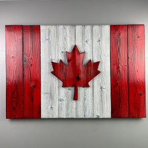 Peut inclure: Un drapeau canadien en bois avec une feuille d'érable rouge au centre. Le drapeau est fait de planches de bois individuelles peintes en rouge et blanc.