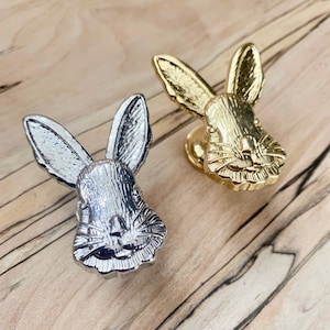 May include: Two rabbit-shaped cabinet knobs, one in silver and one in gold. The rabbit's faces are detailed with fur and whiskers.