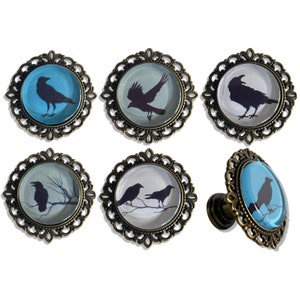 May include: Six decorative cabinet knobs with a bronze finish and a glass insert featuring a silhouette of a crow or crows on a blue or white background.