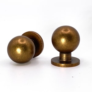 May include: Two antique gold cabinet knobs with a round ball shape and a flat base.