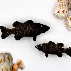 May include: Two wooden bass fish silhouettes, one larger than the other, are displayed on a white background. The larger fish is approximately 25 cm long and the smaller fish is approximately 12.5 cm long. Both fish are painted black.