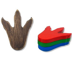 May include: Wooden dinosaur footprint and a stack of three colorful, red, green, and blue, wooden shapes. The footprint is a dark brown color with wood grain. The shapes are stacked on top of each other.