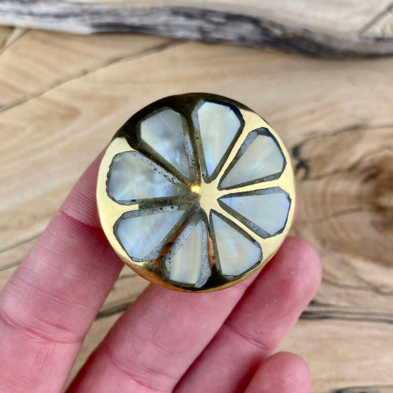 May include: A round brass knob with a white mother-of-pearl inlay in the shape of a flower.