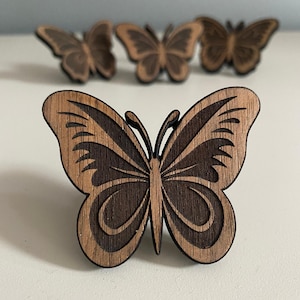 Peut inclure: Quatre ornements en bois en forme de papillon de couleur brun foncé. Les papillons sont finement sculptés avec des motifs d'ailes détaillés.