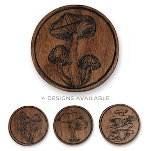 May include: Wooden coasters with engraved mushroom designs. The coasters are round and feature detailed illustrations of various mushroom types. The text "4 DESIGNS AVAILABLE" is displayed below the coasters.