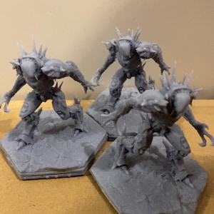Puede incluir: Tres figuras en miniatura grises impresas en 3D de una criatura con púas y garras afiladas de pie sobre bases hexagonales.